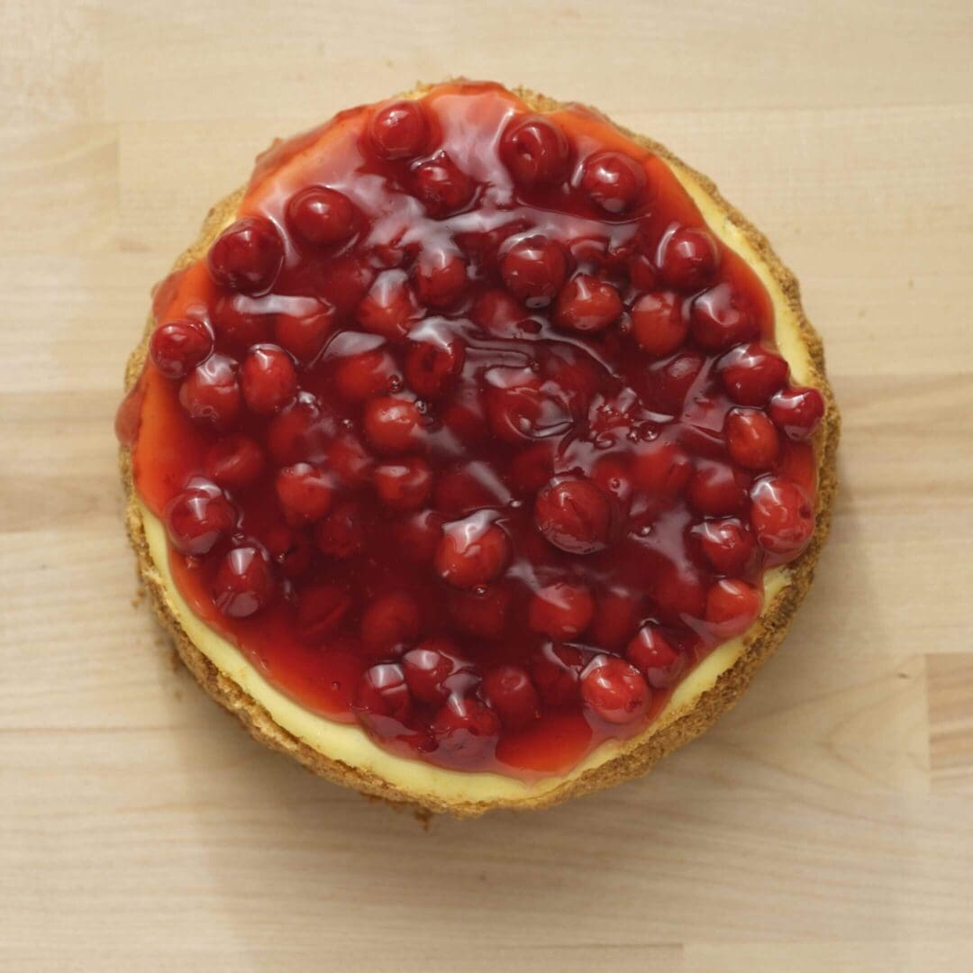 Cherry-topped cheesecake on wooden surface.