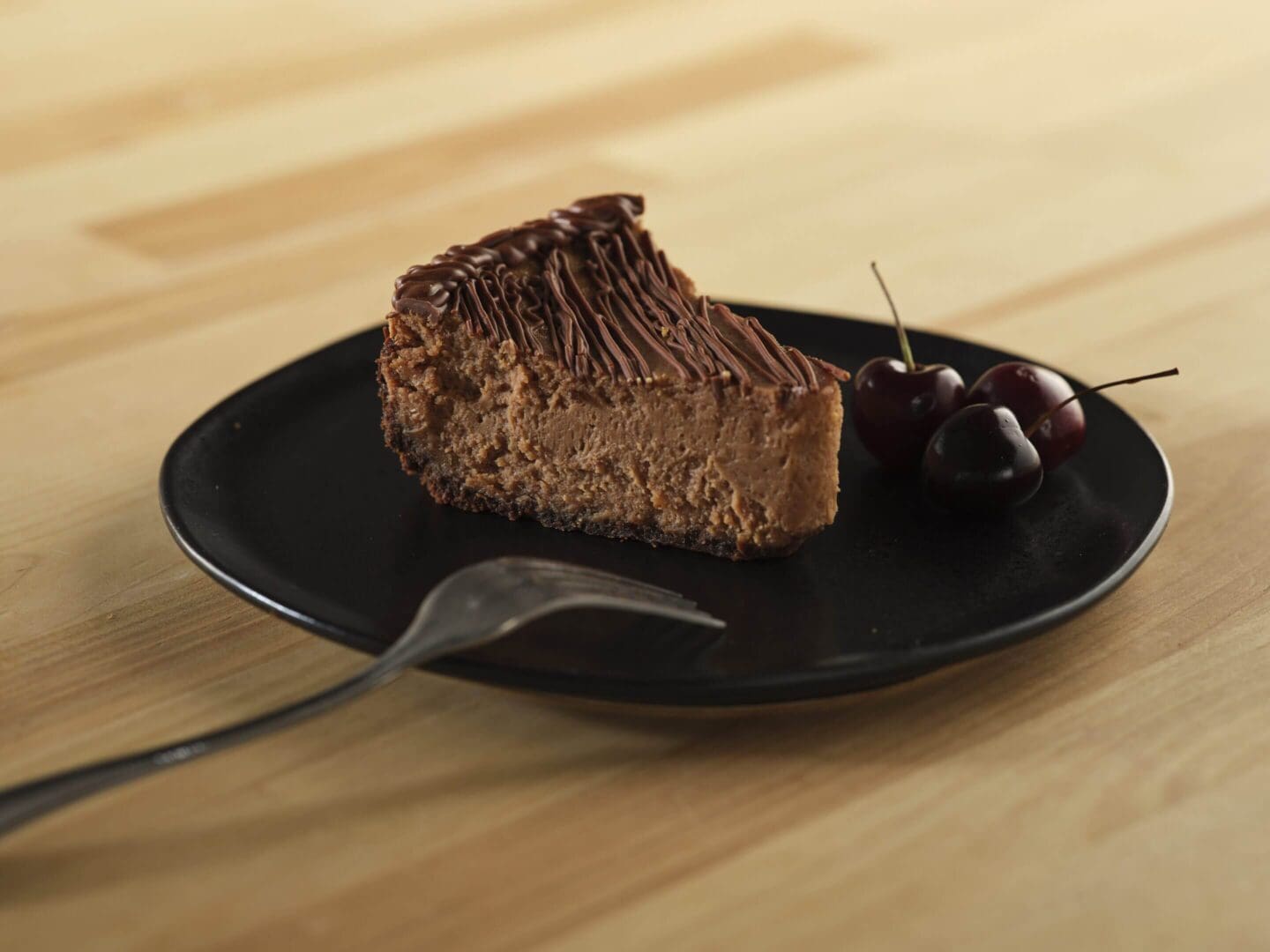 Chocolate cheesecake slice with cherries on plate.