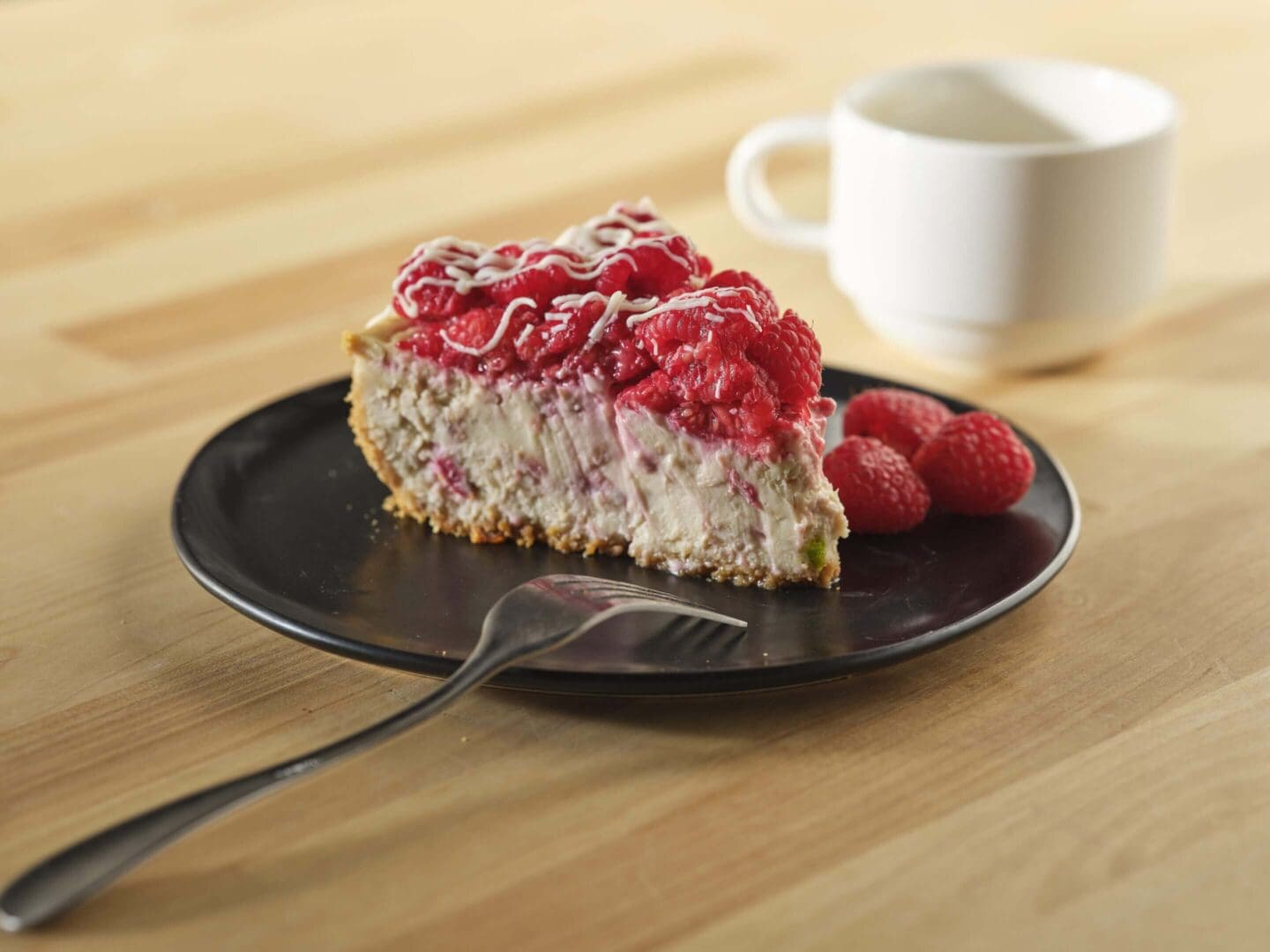 Slice of raspberry cheesecake with coffee cup.