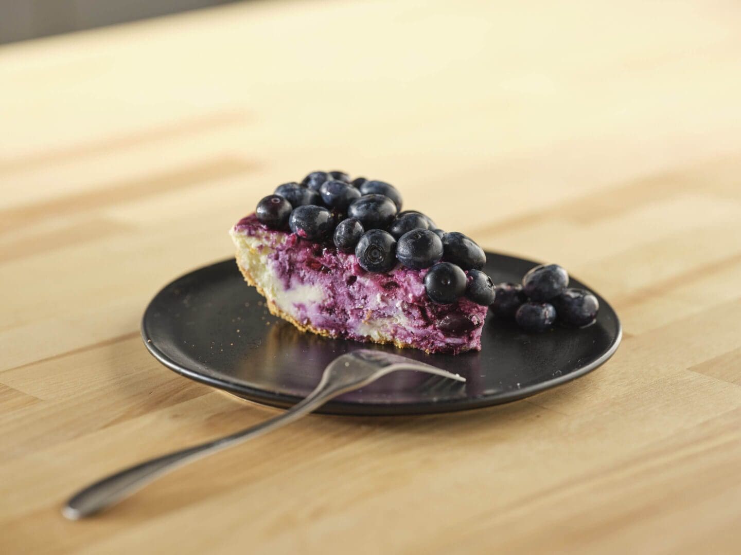 Blueberry cheesecake slice on a black plate.