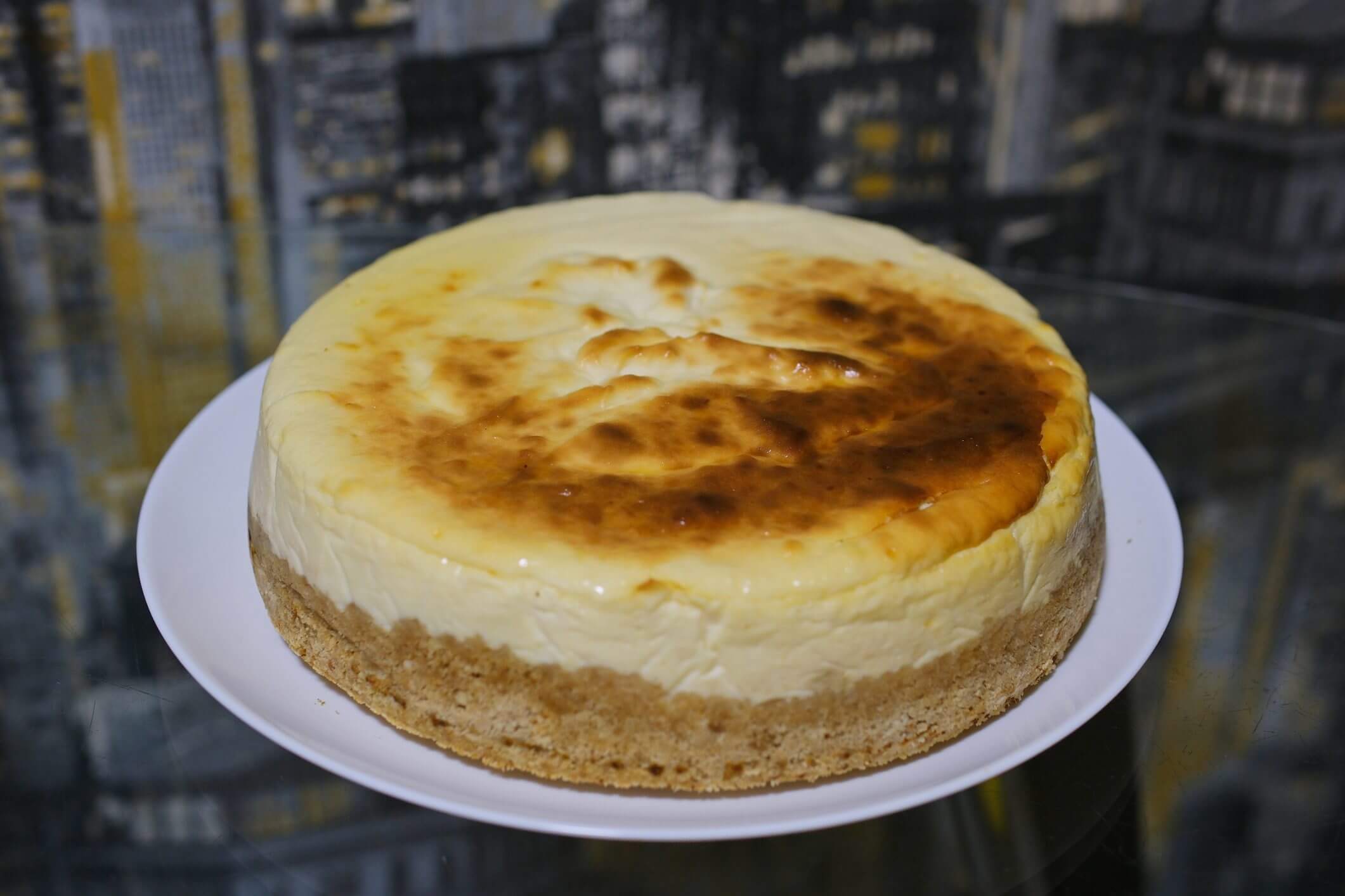 Cheesecake on a white plate, city backdrop.